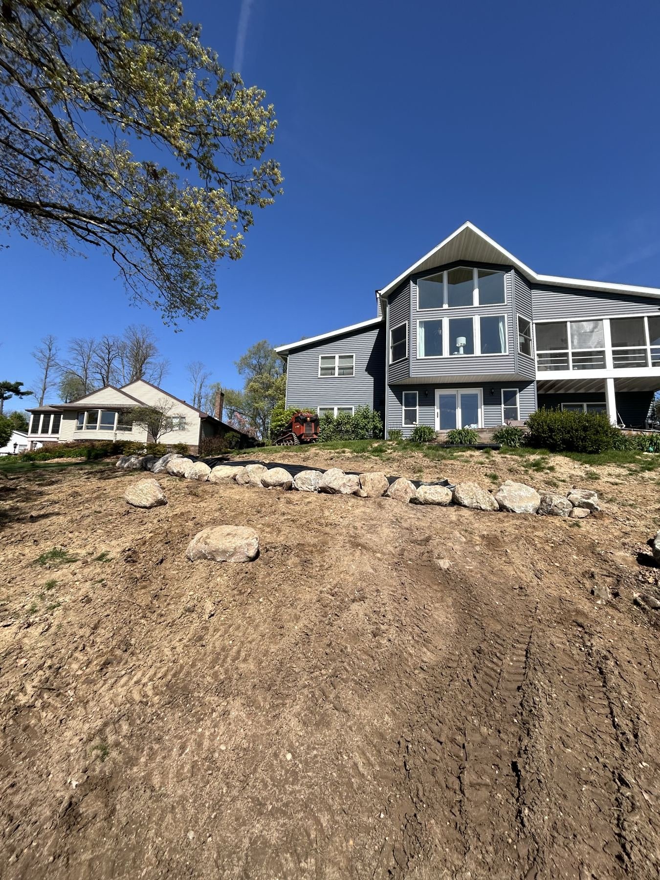 Before: bare graded dirt hillside below a lakefront home