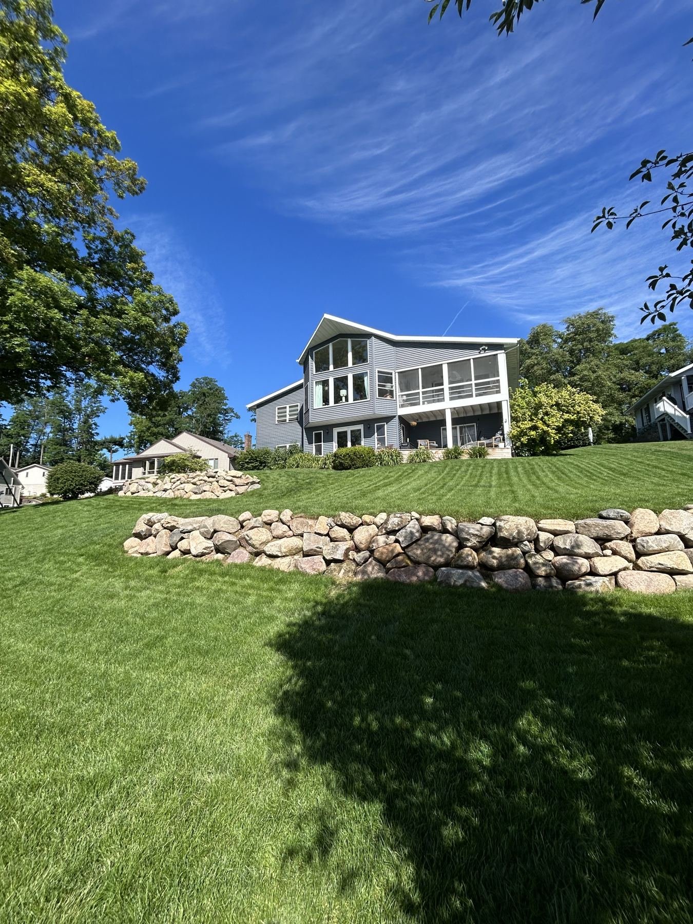 Two-tier natural boulder retaining wall with a freshly striped lawn below a lakefront home